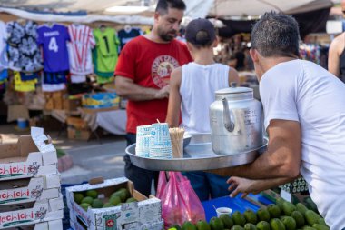 03.08.2024 Antalya, Türkiye - Pazar. Tepsisi ve çaydanlığı olan bir garson Antalya 'da bir pazarda tüccarlara çay doldurur.