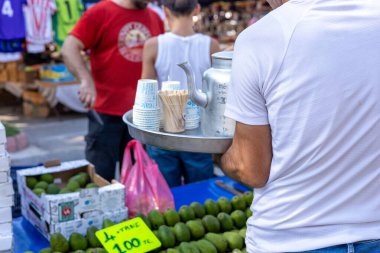 Antalya, Türkiye - 3 Ağustos 2024 - Pazar. Tepsisi ve çaydanlığı olan bir garson Antalya 'da bir pazarda tüccarlara çay doldurur.