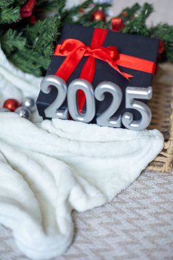 Üzerinde gri sayılar olan dikey bayram nötr kartı, Noel ve yeni yıl kutlamaları, gümüş figürler, yumuşak beyaz ekose, kırmızı fiyonklu siyah hediye kutusu ve arka planda Noel ağacı, kopyalama alanı