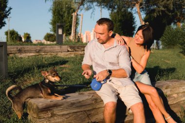 Bir köpekle yürüyen mutlu bir çift, parkta sarılıp öpüşüyor yaz günbatımında, erkek ve kadın portresi, birlikte kolay ve keyifli bir zaman, büyük bir yaş ile ilişki kavramı