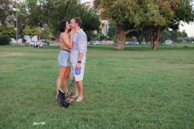 Bir köpekle yürüyen mutlu bir çift, parkta sarılıp öpüşüyor yaz günbatımında, erkek ve kadın portresi, birlikte kolay ve keyifli bir zaman, büyük bir yaş ile ilişki kavramı