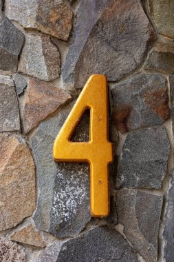 Taş bir duvardaki dört numaralı sarıya yakın çekim. Parlak turuncu figür 4, kır otelinde bir oda ya da ev numarası. Doğal malzemeler ve çevre dostu stil. Yüksek kalite fotoğraf