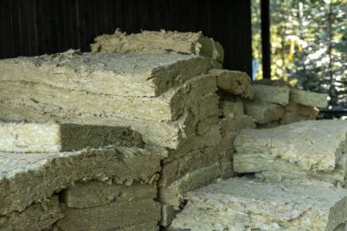 Yalıtım malzemesi yığınları kırsal bir ahır içinde düzgünce düzenlenmiştir. Ahırlardan akan doğal ışık yalıtımın dokusunu ve katmanlarını ön plana çıkarıyor.