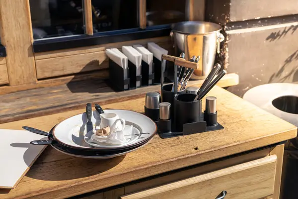 stock image Dirty dishes on a table after client in restaurant. An inviting outdoor cafe, wide variety of knives, a small cup, and utensils on a wooden table, warm and welcoming atmosphere for patrons.