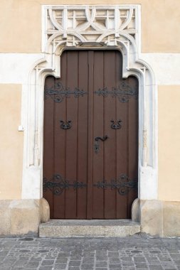 A beautifully crafted wooden door featuring an intricate ornate glass transom sits in a charming historical building in a quaint old town. The door showcases rich tones of wood, complemented by subtle clipart