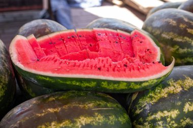 Canlı, taze kesilmiş bir karpuz, yazın hareketli bir çiftçi pazarında tüm karpuzların arasında belirgin bir şekilde bulunur. Tohumlarla lekelenmiş sulu kırmızı et yeşil kabuğa davet ediyor. Güneş ışığı