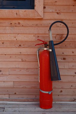 Red classic fire extinguisher stands on the floor outdoors against the background of a wooden wall. Fire safety in a wooden country house clipart