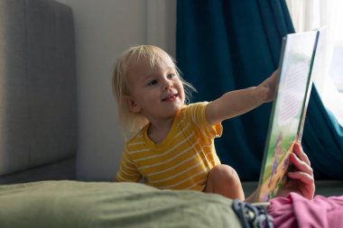 Babamla kitap okurduk. Sarı saçlı neşeli bir çocuk, kötü bir şeyin üzerinde rahatça otururken hevesle bir hikaye kitabını işaret ediyor. Konforlu oturma odası ortamı neşe dolu atmosferi arttırır..