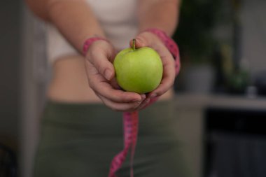 Hands hold a bright green apple, accompanied by a pink measuring tape, suggesting a focus on health and nutrition. Exhaustion due to weight loss and dieting, desire for a slim body concept clipart