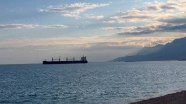 Güneş uzak dağların ardında batarken büyük bir kargo gemisinin sakin sularda yavaşça hareket ettiği görülüyor. Gökyüzü yumuşak bulutlar ve sıcak renklerle boyanır. Huzurlu bir atmosfer yaratır.. 