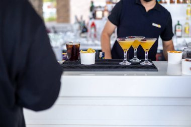 Yetenekli bir barmen yoğun bir bar ortamında lezzetli atıştırmalıklar servis ederken renkli kokteyller hazırlar. Atmosfer canlı, akşam saatlerinde gevezelik ve kahkahalarla dolu..