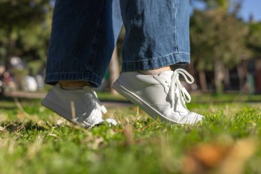 Çıplak ayaklı anatomik ayakkabılar. Taze beyaz ayakkabılar canlı yeşil çimlerin üzerinde dinlenirken bir insan güneşli bir parkta duruyor. Sağlıklı yaşam tarzı ve refah kavramı, sağlık bakımı ve sağlıklı yaşam kavramı