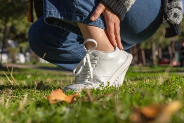 Yalınayak ayakkabılar. Bir insan beyaz spor ayakkabı giyerken yemyeşil çimenlere dikkatle basar. Hafiflik ve esneklik, geniş ayak parmaklı ayakkabılar. Anatomik sağlıklı günlük ayakkabılar.