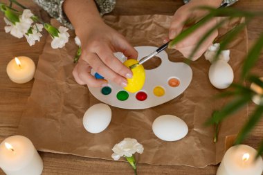 Eller, mum ve çiçeklerle çevrili canlı bir renk paleti kullanarak beyaz yumurtaları dikkatlice boyar. Bu etkinlik, bahar açılırken Paskalya 'nın şenlikli ruhunu yakalar..