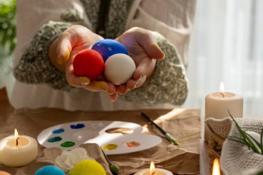 Geleneksel elbiseli kadın, kırmızı, mavi ve beyaz renklerle boyanmış üç Paskalya yumurtası tutarken, daha fazla süslü yumurta, boya, fırça ve mumlarla çevrelenmiş ülke bayrağını simgeliyor.. 
