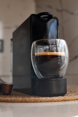 Gösterişli bir kahve makinesi mutfak tezgahında oturup koyu bir espresso hazırlıyor. Evdeki mutfakta şeffaf bardakta Americano hazırlayan kapsüllü kahve makinesi..