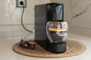 Gösterişli bir kahve makinesi mutfak tezgahında oturup koyu bir espresso hazırlıyor. Evdeki mutfakta şeffaf bardakta Americano hazırlayan kapsüllü kahve makinesi..