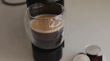 Lezzetli kapsül kahve ustalıkla minik bir kahve makinesinde demlenir. Cam bardak, taze içeceğin kremsi dokusunu ve davetkar kokusunu sergiliyor. Günlük ev rutini ve yaşam