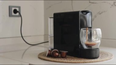 Gösterişli bir espresso makinesi çağdaş bir mutfakta bir fincan taze kahve hazırlar. Parlak sabah ışığı, kullanılmış kahve kapsüllerinin yanındaki zengin espresso bardağını vurgular.