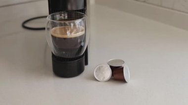 Lezzetli kapsül kahve ustalıkla minik bir kahve makinesinde demlenir. Cam bardak, taze içeceğin kremsi dokusunu ve davetkar kokusunu sergiliyor. Günlük ev rutini ve yaşam