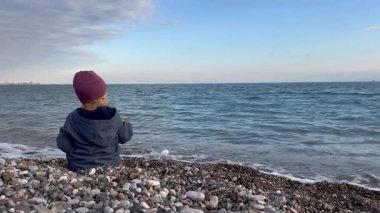 Küçük bir çocuk bir çakıl taşı plajında oturur, sakin okyanusu ya da deniz dalgalarını işaret eder. Sahne, Türkiye 'de deniz kenarında güneşli bir kış gününde çocukluk sevincini yakalıyor..