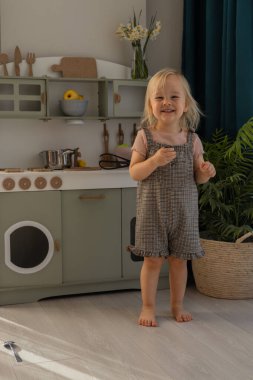 Çocuk, dekore edilmiş, aydınlık bir odada mutfak oyuncaklarıyla oynarken gülümsüyor. Minyatür mutfak çeşitli mutfak aletleri ve renkli eşyalar içeriyor. Çevre dostu ve güvenli el yapımı.