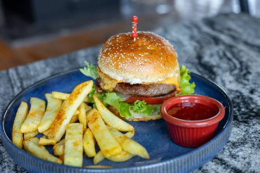 Mavi tabakta kızarmış patatesli bir Amerikan hamburgeri. Sağlıksız gıda konsepti. Kafede ya da restoranda çizburger ve patates kızartması, fast food. 