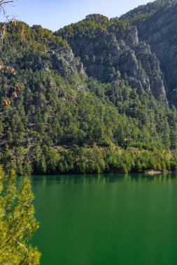 Sakin bir göl, yüksek dağları ve sık çam ağaçlarını yansıtır. Berrak mavi sular rahatlamaya, gösterişli doğaya ışık altında güzellik sunmaya davet eder..