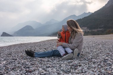 Bir anne ve oğlu kışın çakıl taşı plajında oturur, arka planda denizi ve dağları seyrederler. Soğuk hava neşeli anlarına dingin bir atmosfer katıyor..
