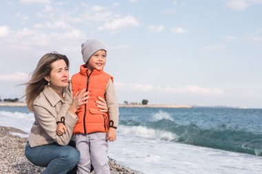 Bir anne ve küçük oğlu kışın çakıllı bir plajda birlikte dururlar. Dalgalar nazikçe ayaklarına vururken birbirlerine gülümserler ve gökyüzü yumuşak bulutlarla açıktır. Aile yaşam tarzı