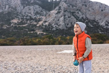 Bir anne ve oğlu soğuk bir kış gününü plajda geçiriyorlar. Parlak turuncu bir yelek ve gri bir bere takan çocuk, kırmızı bir top tutuyor, gülümsüyor ve etrafını güzel dağlarla çeviriyor..