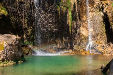 Su kayalık bir uçurumdan aşağı dökülür ve berrak bir turkuaz havuza akan çarpıcı bir şelale oluşturur. Yeşillik, ormanı çevreleyerek ormandaki sakin atmosferi güçlendirir..