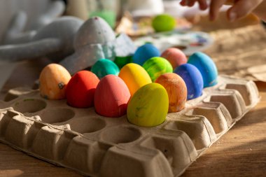 Lüks bir tavşan yumurta kutusunun üzerinde duran canlı Paskalya yumurtalarının yanında yatar. Güneş ışığı, neşeli renkleri ve bahar şenliklerinin ılık atmosferini vurguluyor..