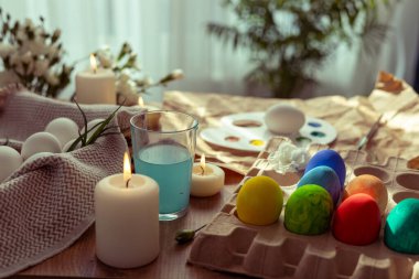 Pastel renkli Paskalya yumurtaları, mumlar ve doğal dekorlarla süslenmiş bir masa bahar kutlaması için ortam hazırlar. Etkinlik yumurta süslemeyi ve neşeli bir atmosfer yaratmayı içeriyor..