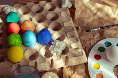 Pastel renkli Paskalya yumurtaları, mumlar ve doğal dekorlarla süslenmiş bir masa bahar kutlaması için ortam hazırlar. Etkinlik yumurta süslemeyi ve neşeli bir atmosfer yaratmayı içeriyor..