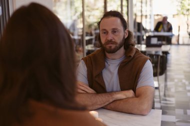 İki birey, çift, kafede yan yana oturur, rahat atmosferin tadını çıkarırlar. Dostum, sakallı ve günlük kıyafetli, içerde arkadaşınla veya sevgilinle konuşurken gülümsüyor..