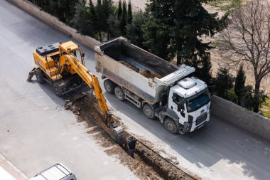 Türkiye, Antalya - 10.03.2025: inşaat ekibi kazı makinesi ve çöp kamyonu kullanarak caddeyi aktif olarak onarıyor. Kamyon yakınlarda park halindeyken işçiler kaldırımları kazmakla meşgul..
