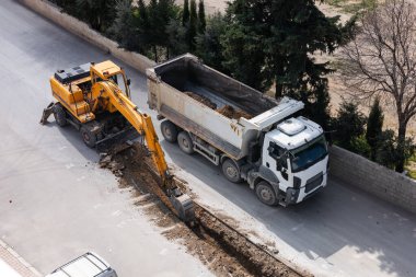 Bir inşaat ekibi kazı makinesi ve çöp kamyonu kullanarak caddeyi onarıyor. Yol tamiri ya da boru tamiri. Hava görünümü