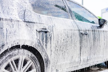 Kalın sabun köpüğüyle kaplı bir araba yerel bir benzin istasyonunda park halinde. Yüzeyden su damlıyor ve işçiler gün ışığında onu tamamen temizlemeye hazırlanıyorlar. Otomobil yıkama işlemi