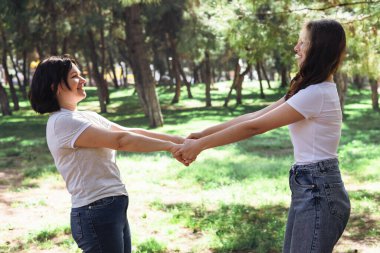 İki kadın anne ve kız yeşil parkta ya da ormanda durup neşeyle el ele tutuşup gülüyorlar. Gündelik giysiler giyip güneşli bir günün tadını çıkarırken aynı zamanda eğlenceli aile anlarını paylaşıyorlar..