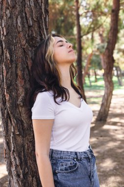 Genç bir kadın ormanda bir ağaca karşı, gün ışığının tadını çıkararak huzur içinde duruyor. Gözlerini kapatır, doğanın tadını çıkarır sükunet, sade beyaz bir gömlek ve kot pantolon giyer..