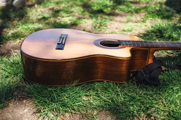 Akustik bir gitar yeşil çimlerin üzerinde uzanır, güneşli bir günün sıcak güneş ışığını yakalar. Dostlar yakınlarda toplanır, müzik ve sohbetin tadını çıkarırlar..