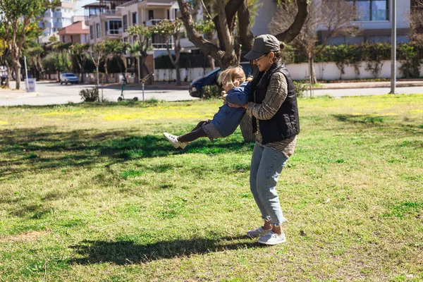 Kadın büyükannesi, genç kızıyla canlı yeşil parkta eğlenmekten zevk alıyor. Güneş, öğleden sonraları ağaçlar ve açık alanla çevrili bir şekilde gülüşlerini paylaşırken ışıl ışıl parlıyor..