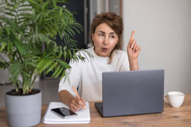 Evde dizüstü bilgisayar eğitimi alan, not defterine notlar yazan, internet üzerinden eğitim gören, profesyonel kurslar alan, sesli dersler dinleyen, ciddi ve olgun bir kadın.