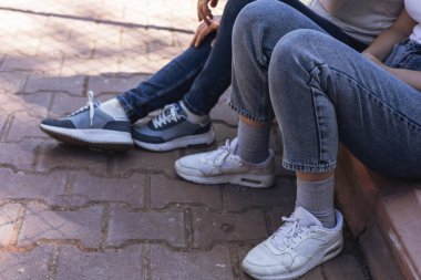 İki arkadaş parkta güneşli bir günün keyfini çıkarıyorlar. Kotlar ve rahat spor ayakkabılar giyiyorlar. Taş bir yolda oturup sohbet eder ve birbirlerine eşlik ederler..