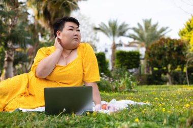 Sarı elbiseli güzel esmer kadın dizüstü bilgisayarla parkta oturuyor. Artı, internette çalışan ya da okuyan kadın sayısı, serbest çalışan. Gülümseyen şişman kadın dışarıda yaz gününün tadını çıkarıyor.