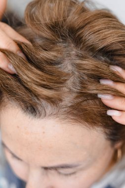 Olgun orta yaşlı beyaz kadın gri, gümüş kökü kıllarına dokunuyor arka plandaki gri fayanslar, saç dökülmesi ve yaşla ilgili değişiklikler, doğallık ve doğal yaşlanma konsepti.. 