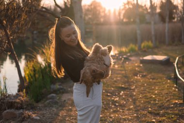 Küçük köpeğini kucaklayan ve kucaklayan genç kadın, cocker spaniel cins köpek yavrusu. Kamu parkında altın gün batımı, evcil hayvanlarla açık hava aktiviteleri