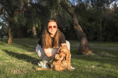 Parlak yeşil bir parkta duran bir kadın cocker spaniel köpeğiyle meşgul oluyor. Köpek hevesle oturup güçlü bağlarını ve neşeli atmosferini gösterirken o oyuncağı tutuyor..