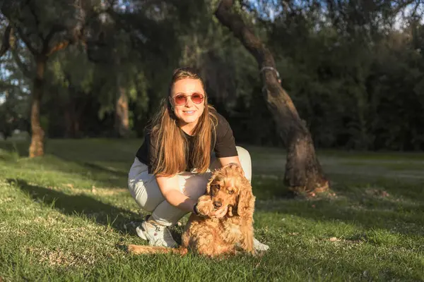 Parlak yeşil bir parkta duran bir kadın cocker spaniel köpeğiyle meşgul oluyor. Köpek hevesle oturup güçlü bağlarını ve neşeli atmosferini gösterirken o oyuncağı tutuyor..